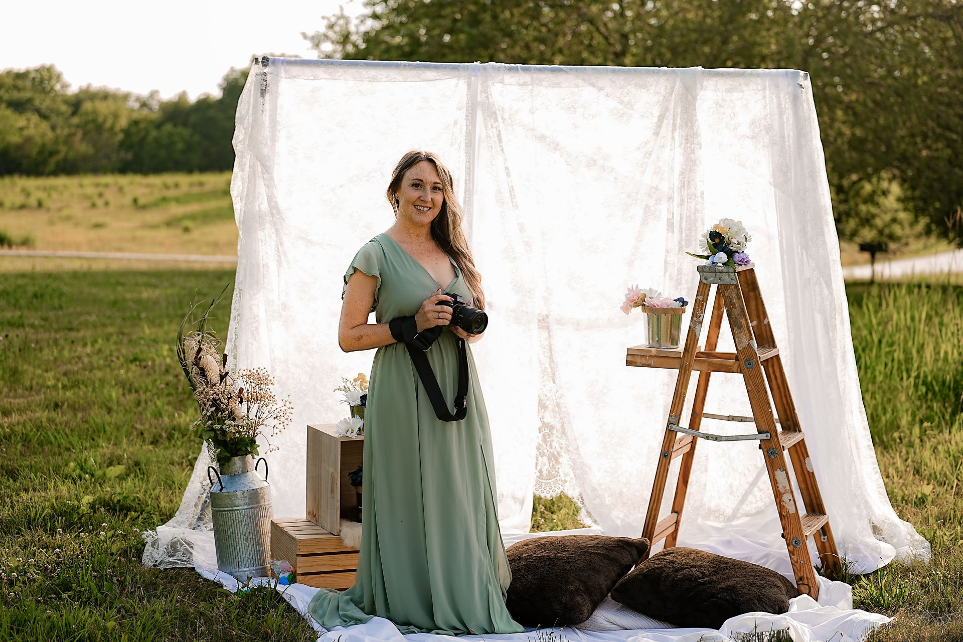 Des Moines, Iowa professional photographer - a woman with long blonde hair and a long green dress is standing in front of a white lace sheet holding a Sony camera.