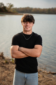 Calli Tuggle Photography - Des Moines, Iowa area senior photographer - a male high school senior wearing a black t-shirt and jeans crosses his arms in front of a lake.