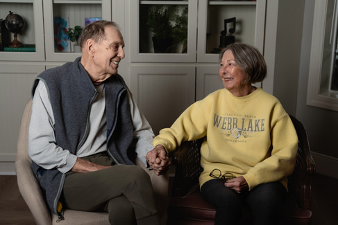 Des Moines, Iowa portrait photographer - Calli Tuggle Photography - elderly couple holds hands with one another and looks at each other lovingly while sitting in front of a white bookcase.
