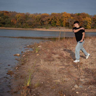 Des Moines and Norwalk, Iowa high school senior photographer - male teenager in a black t-shirt and jeans skips rocks on a sandbar.