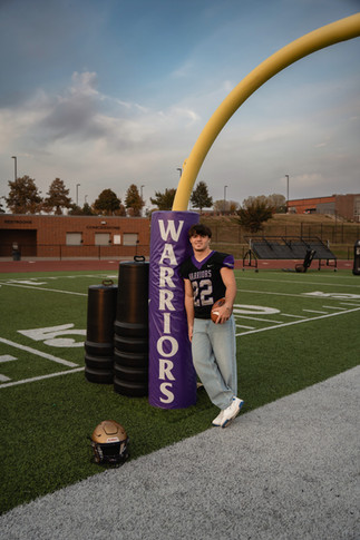 Norwalk and Des Moines, Iowa high school senior photography - football player stands on the field wearing his jersey and jeans leaning against the goal post.
