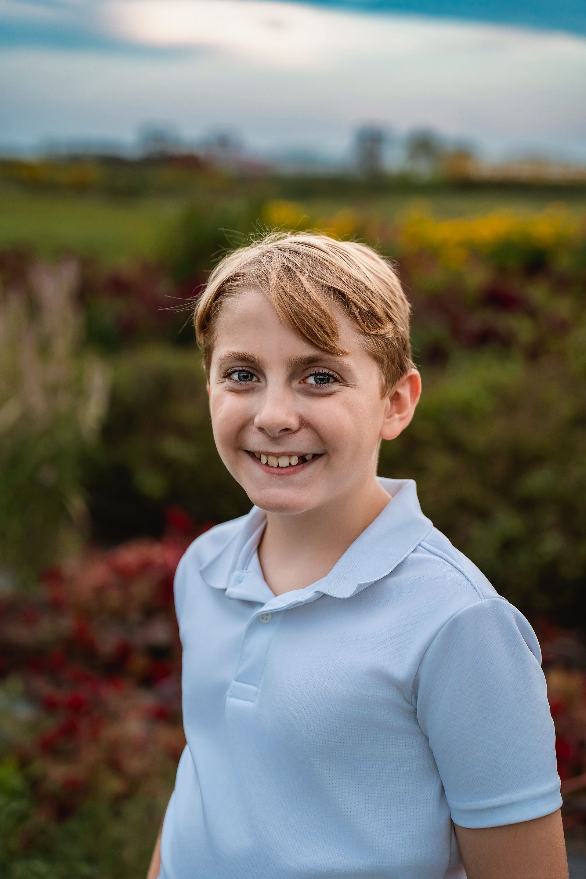 Des Moines and Norwalk, Iowa family photographer - pre-teen boy in a white polo smiles in a flower field.