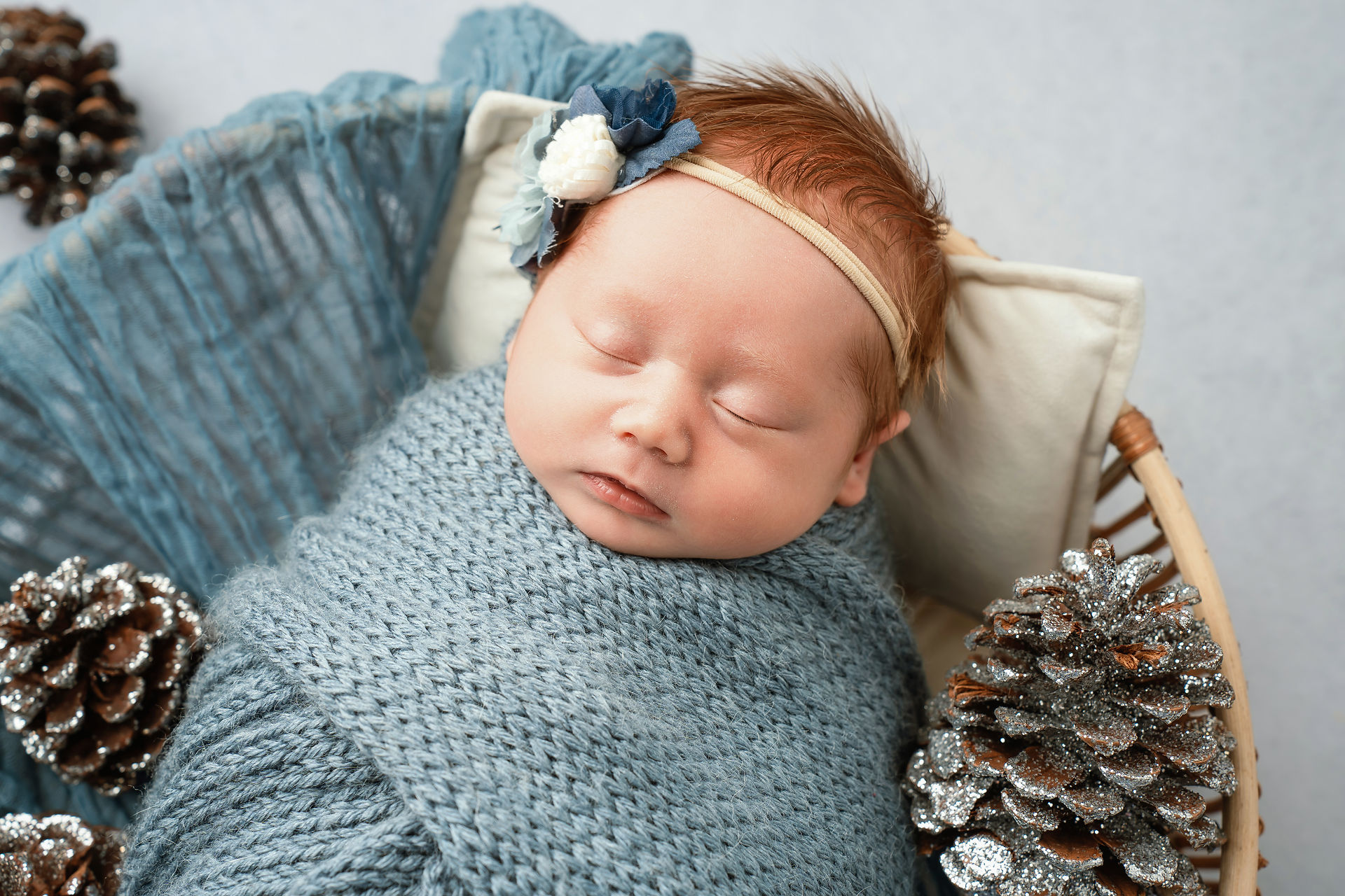 Des Moines and Norwalk, Iowa newborn photography - a newborn baby girl with red hair is swaddled in a blue knit blanket 