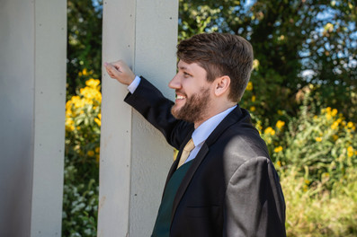 Central Iowa wedding photographer - Groom leans against a post smiling.
