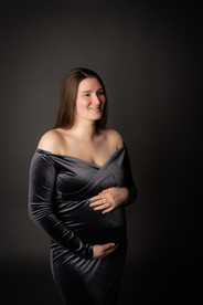 Des Moines, Iowa maternity and newborn photographer - a pregnant woman wears an off the shoulder dark velvet dress in front of a dark backdrop.