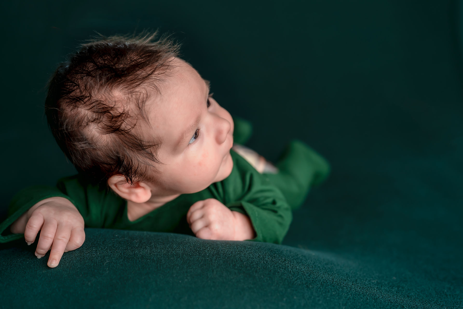 Des Moines, Iowa Newborn Photographer - newborn baby boy lying on tummy in green outfit on green background looking away