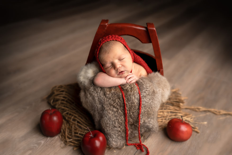 Des Moines, Iowa Newborn Photographer - newborn baby girl is wearing a red bonnet and is posed inside a red bucket surrounded by red apples.