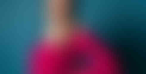 Des Moines and Norwalk, Iowa pregnancy photos - woman with long dark hair and bright pink maternity gown with flowy sleeves poses in front of a blue backdrop.