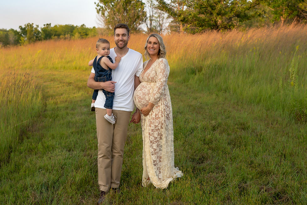 Des Moines and Norwalk, Iowa Family Photographer - a family of three (man, pregnant woman, and toddler) are standing in a prairie.