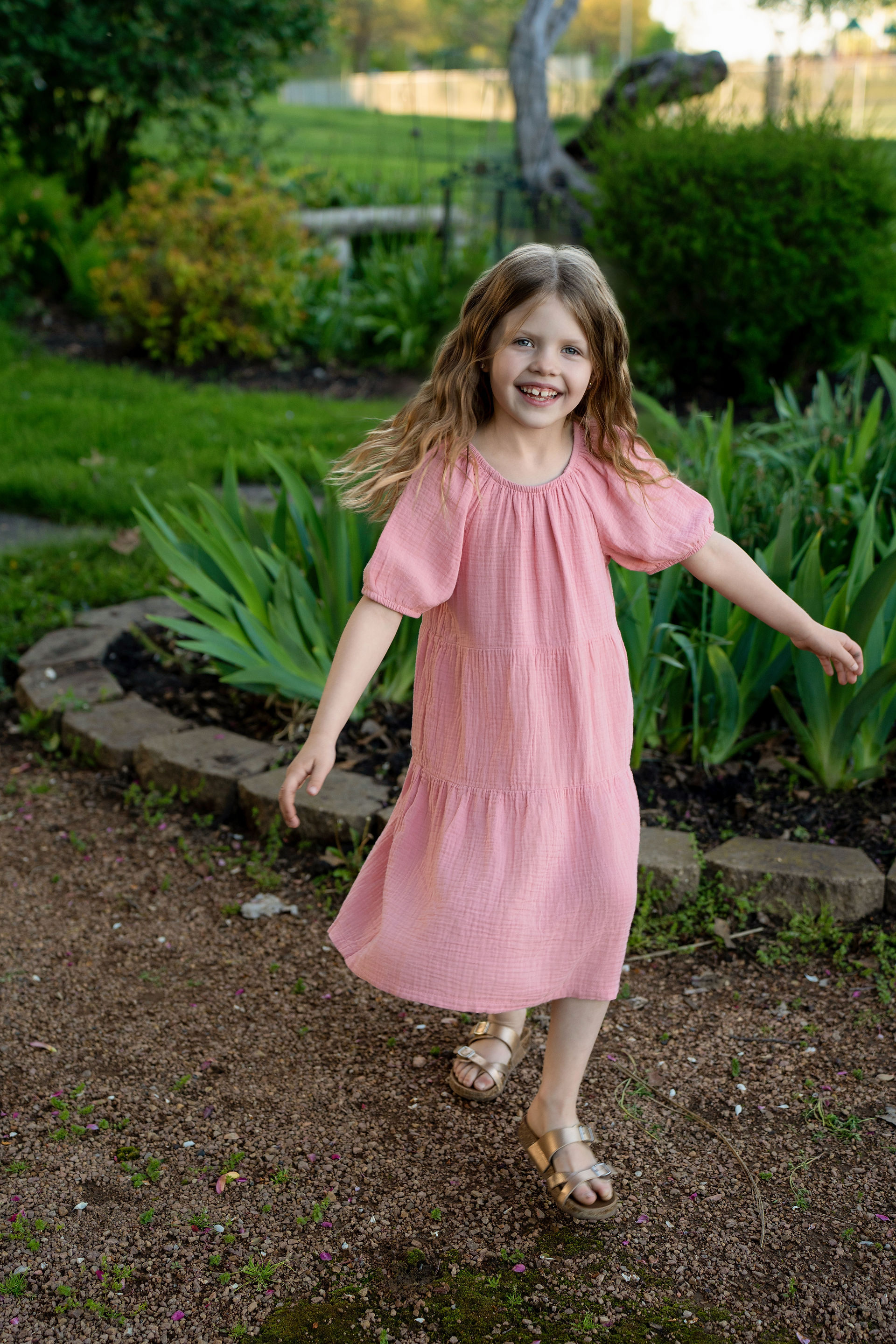 Des Moines, Iowa family photographer - school-aged girl in a pink dress twirling in a flower garden during sunset
