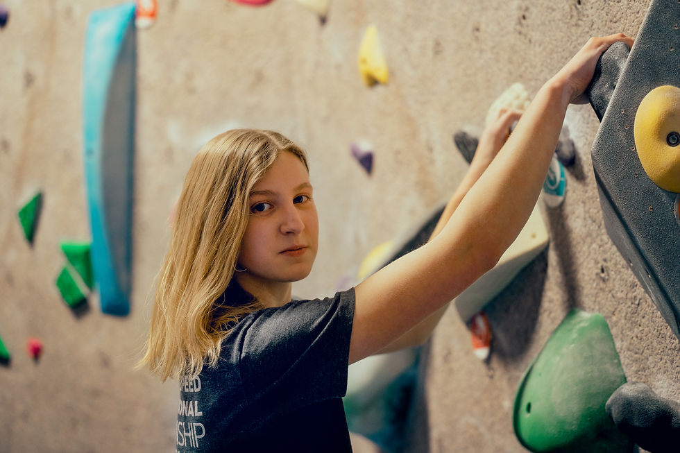 Des Moines, Iowa Photographer - Colored image of teenage girl with long blonde hair and a black t-shirt rock wall climbing at an indoor location.