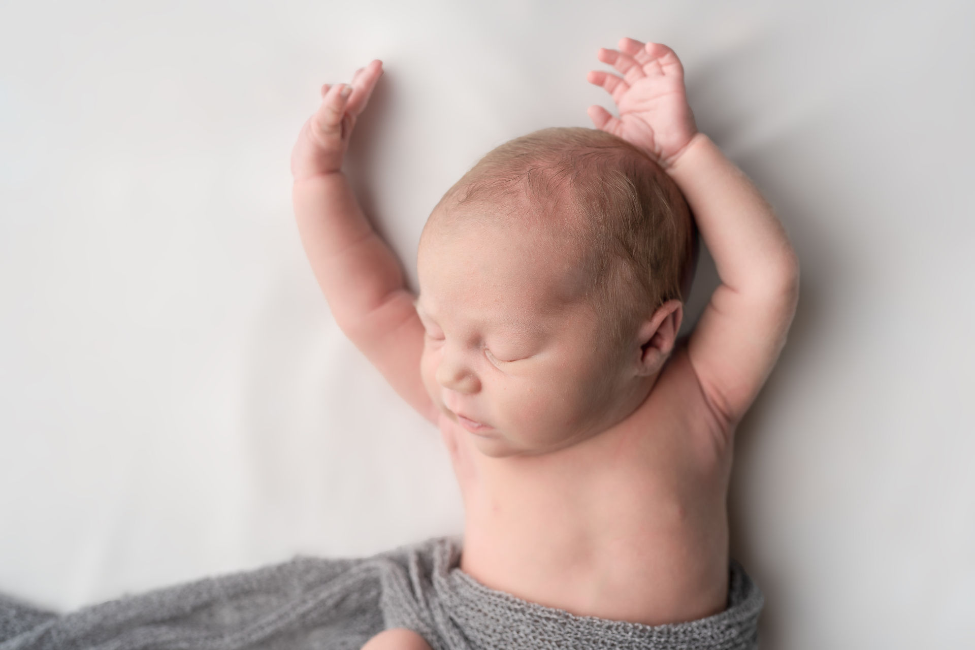 Des Moines, Iowa newborn photographer - a photo of an infant baby girl on a white backdrop asleep with her hands raised above her head.