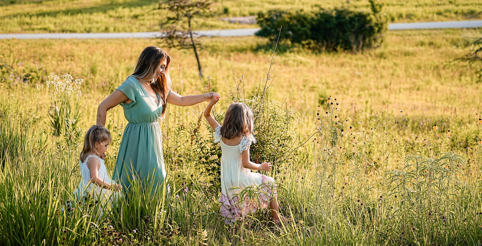 Des Moines, Iowa Family Photographer - a mother and her two daughters are holding hands and walking through an Iowa prarie during golden hour.