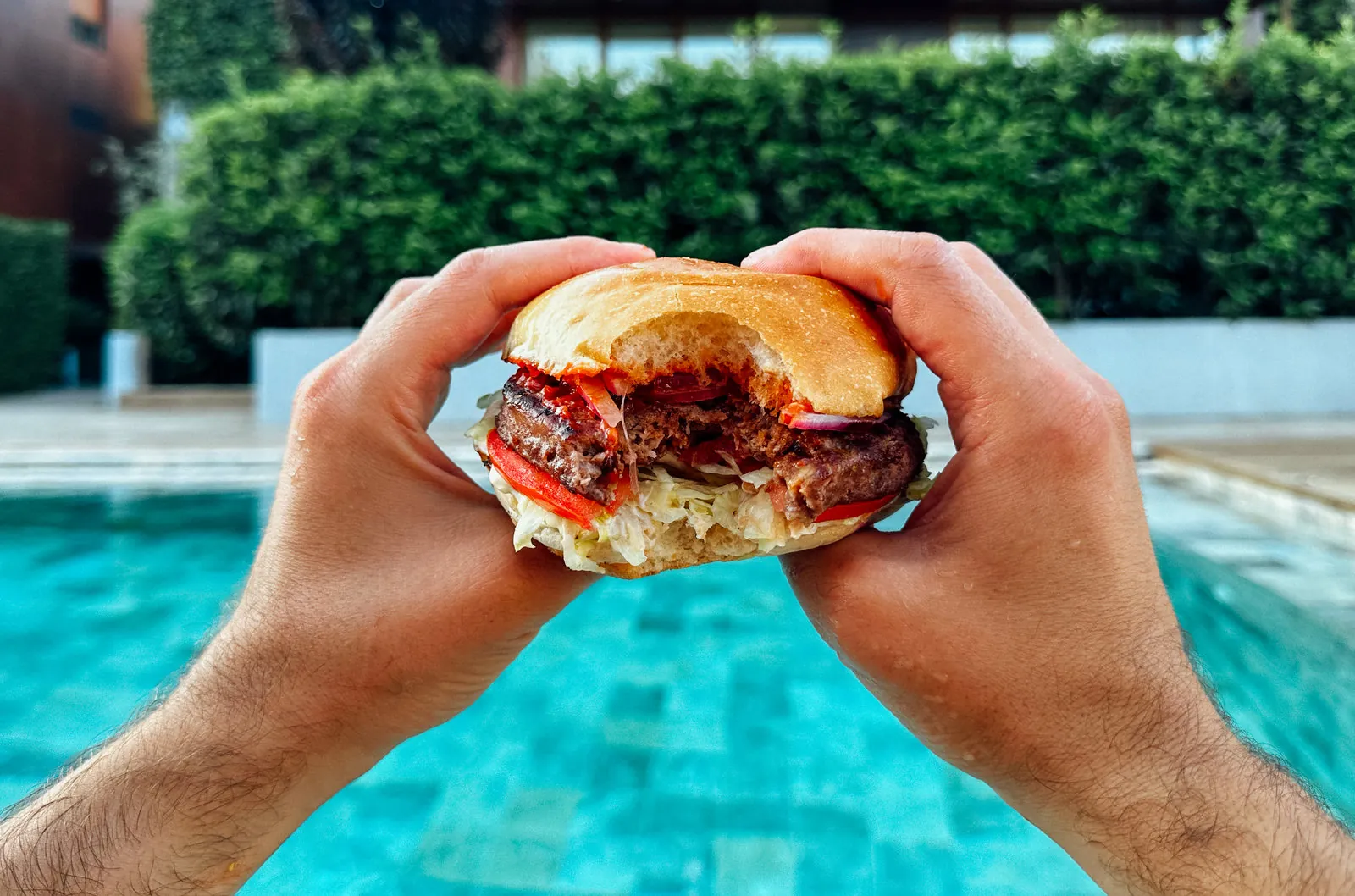Havuz kenarında iki elle tutulan YOKET bitkisel burger