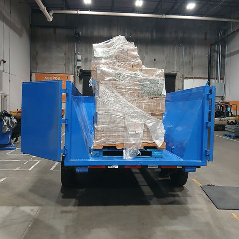 A blue trailer is inside of a warehouse with open double doors. Inside the trailer are various boxes on top of a pallet, wrapped in plastic wrap.
