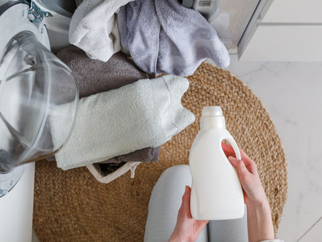 Person holding a non-labeled plastic container of laundry soap near open machine with towels