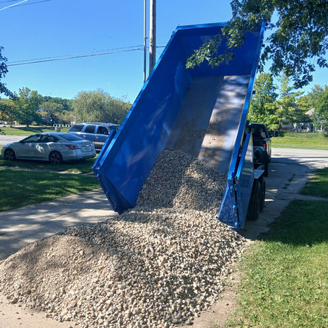 Lifted blue trailer dumping landscaping rocks onto the ground.