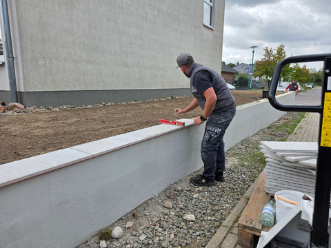 Unser Mitarbeiter richtet eine Keramik-Abdeckplatte auf der Mauer aus.