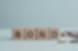 4 wooden cubes in a row spelling out bonds next to coins on a table.