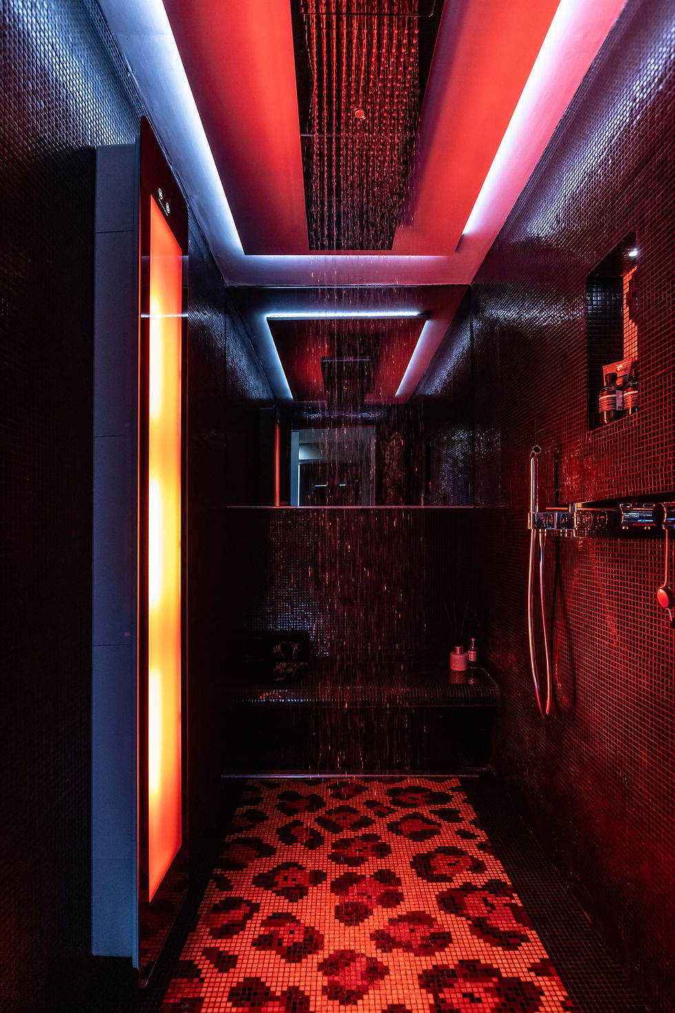 Dim red-lit modern shower room with Axor Heaven + Sunshower waterfall shower heads, mosaic tile walls, and patterned floor, creating a sleek spa mood
