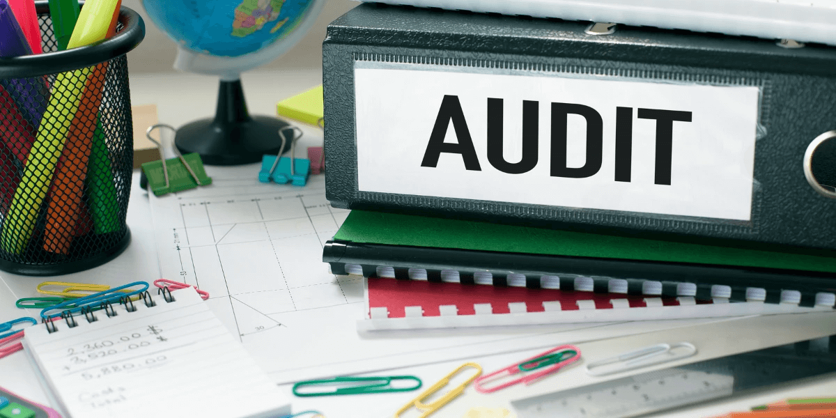 A binder with a printed 'AUDIT' label; charts, pads, and pens on top of a desk