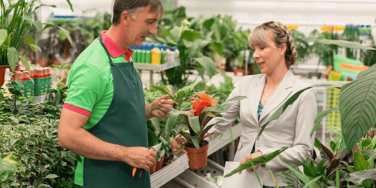 Older male staff at a garden center advising a female buyer on what plants will thrive in her garden