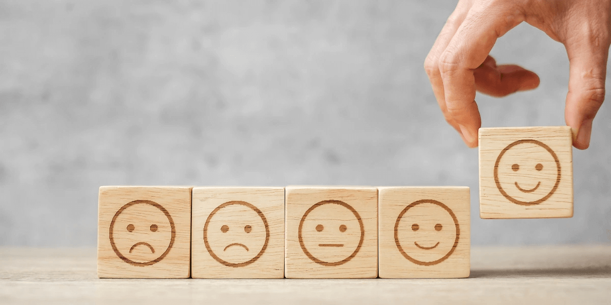 Wooden blocks showing different face emotions. Hands picking up the happy block to denote customer satisfaction
