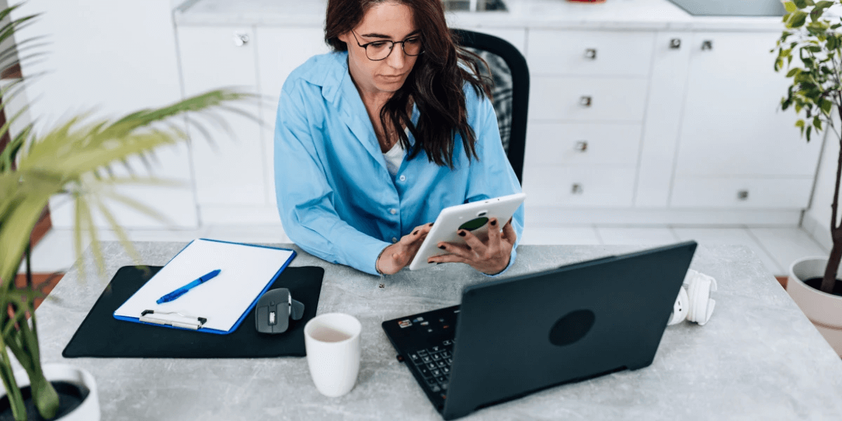 A business owner in her office in front of a laptop and holding her tablet to optimize her company's Google My Business profile for SEO