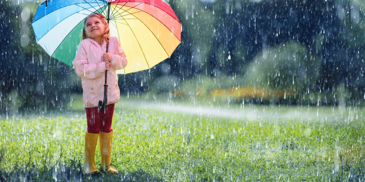 A happy child with a rainbow umbrella under the rain