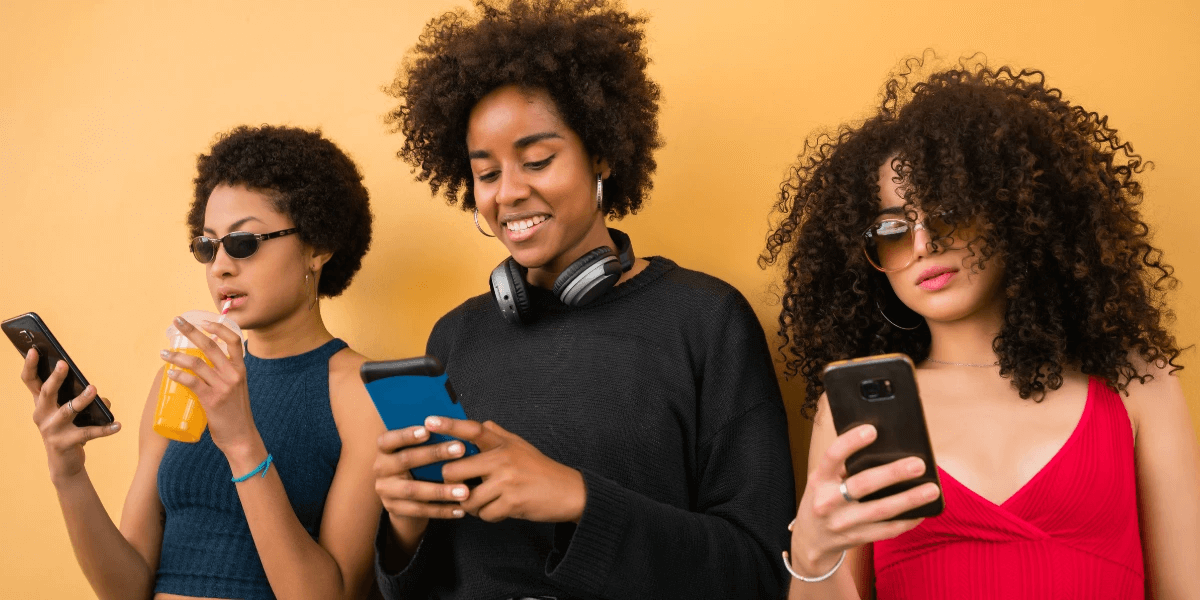 Three friends standing together using their mobile phones