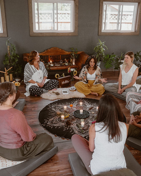 Dori Lewis speaks to a group of students who are seated cross legged on cushions in a circle around a geometric center altar/mandala.