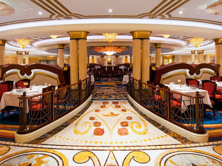 Royal Palace restaurant on Disney Cruise Line, showcasing elegant chandeliers, golden columns, and marble floors with rose designs. The grand dining room features plush red chairs, white-clothed tables, and a regal ballroom-inspired atmosphere, creating a fairytale dining experience at sea.
