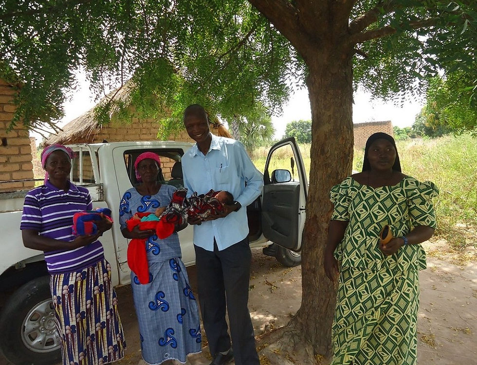 Le président de la Maison des Orphelins et des Enfants des Rues du Tchad se tient à l'extérieur, sous un grand arbre, portant les triplés nourrissons aux côtés de leur mère, de leur grand-mère et de leur tante, lors d'une transition réussie de notre centre de soins à leur domicile résidentiel après avoir assuré un transport sécurisé.