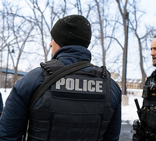 Three police officers outdoors, one wearing a 'POLICE' vest.