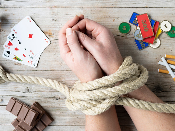 Hands of man are tied and lie on light wooden background surrounded by various symbols of