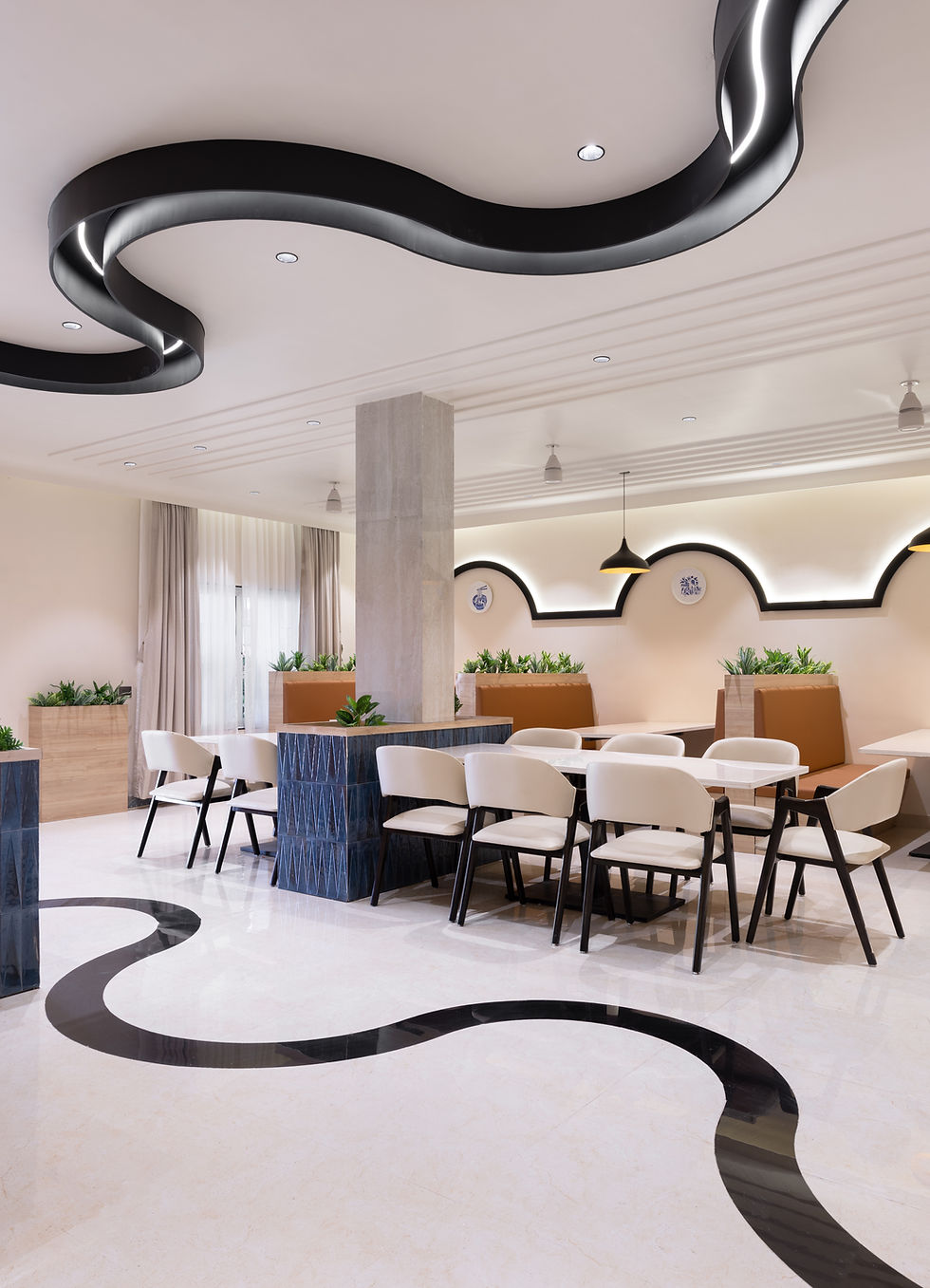 Modern dining room with white chairs, marble tables, black wave ceiling lights, plants, and cream walls in a calm setting