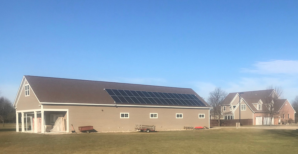 Solar panels atop pole barn send electricity to rectory in background.
