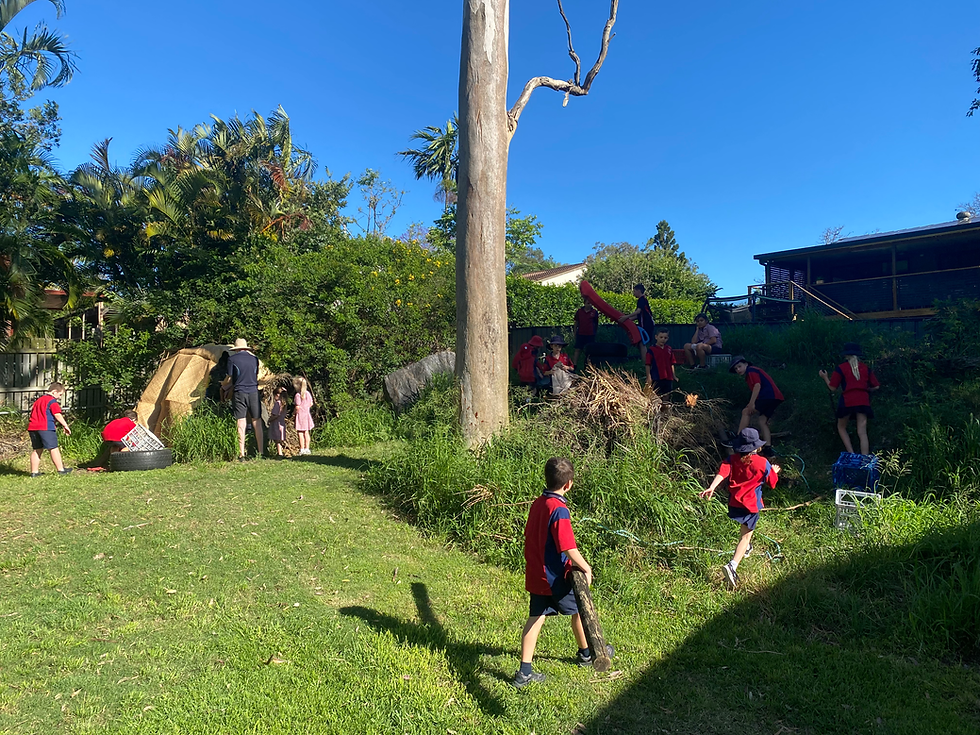 Children playing amongst rocks, trees and grass with loose parts equipment.