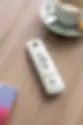 Somfy remote on wood table near a coffee cup with saucer and cookies. Remote has four buttons; subtle, calm setting with soft colors.