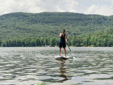 A paddleboarder navigates a river with a forested shoreline behind him