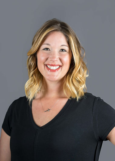 Woman in black shirt, curly blonde hair, pink lipstick, muted purple background.