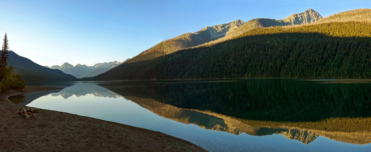 deep shadows on gentle hill reflected in still water of a lake, with mountain peaks far off in the distance