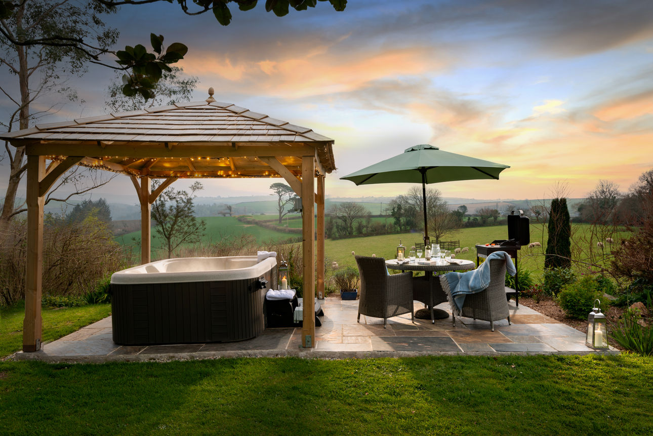 Linhay gazebo covered hot tub, garden furniture with parasol, BBQ and countryside view beyond.