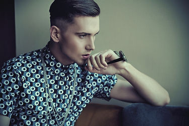 Stylish man poses, wearing patterned shirt, holding watch, looking thoughtful, Gents Hair Styles