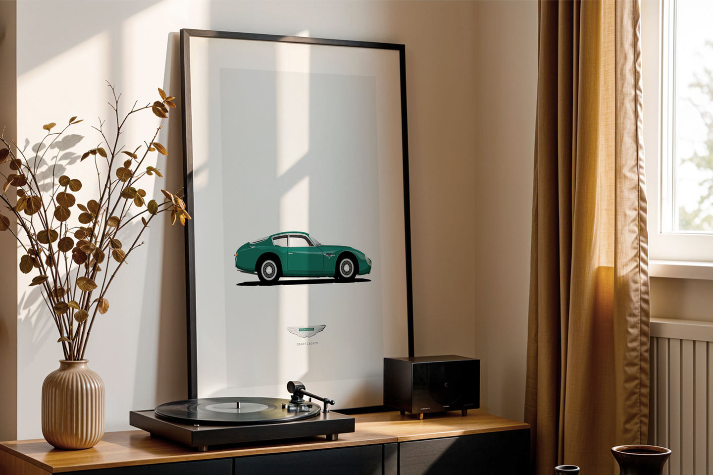 Framed illustration of a green Aston Martin DB4 GT Zagato displayed on a modern sideboard. The artwork leans against a white wall in a stylish, sunlit room. The sideboard also holds a record player, a speaker, a beige vase with dried branches, and books.