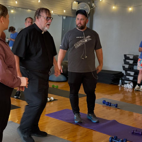 Kevin Farley, playing the role of Father Joseph, leads a workout session on the set of Pickleball: The Movie.