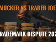 Gavel above jars labeled "Smucker vs Trader Joe’s" and "Trademark Dispute 2025," conveying legal conflict. Dark background.