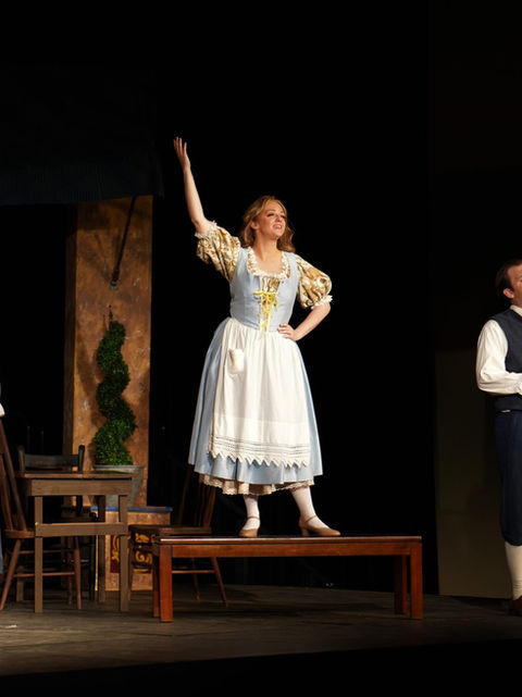 Gillian, standing on a bench with arm raised, as Adina with Mobile Opera in 2022..