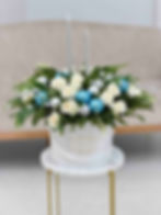Winter holiday flower arrangement with white roses, blue ornaments, silver candles, and greenery in a white Le Boutique Royal
