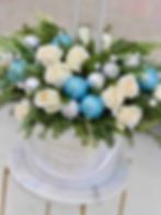 Winter holiday flower arrangement with white roses, blue ornaments, silver candles, and greenery in a white Le Boutique Royal